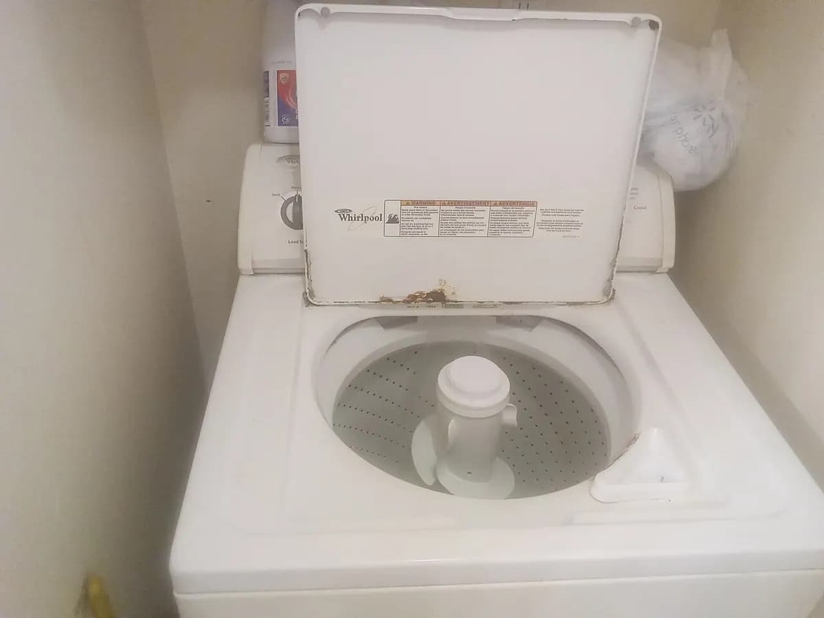 A top-loading washing machine with its lid open, showing the agitator and drum.