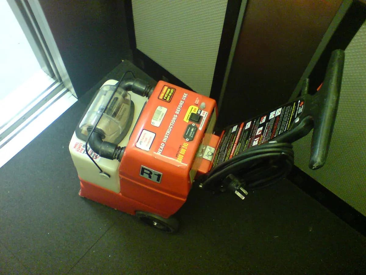 An orange carpet-cleaning machine parked in a hallway beside a window.