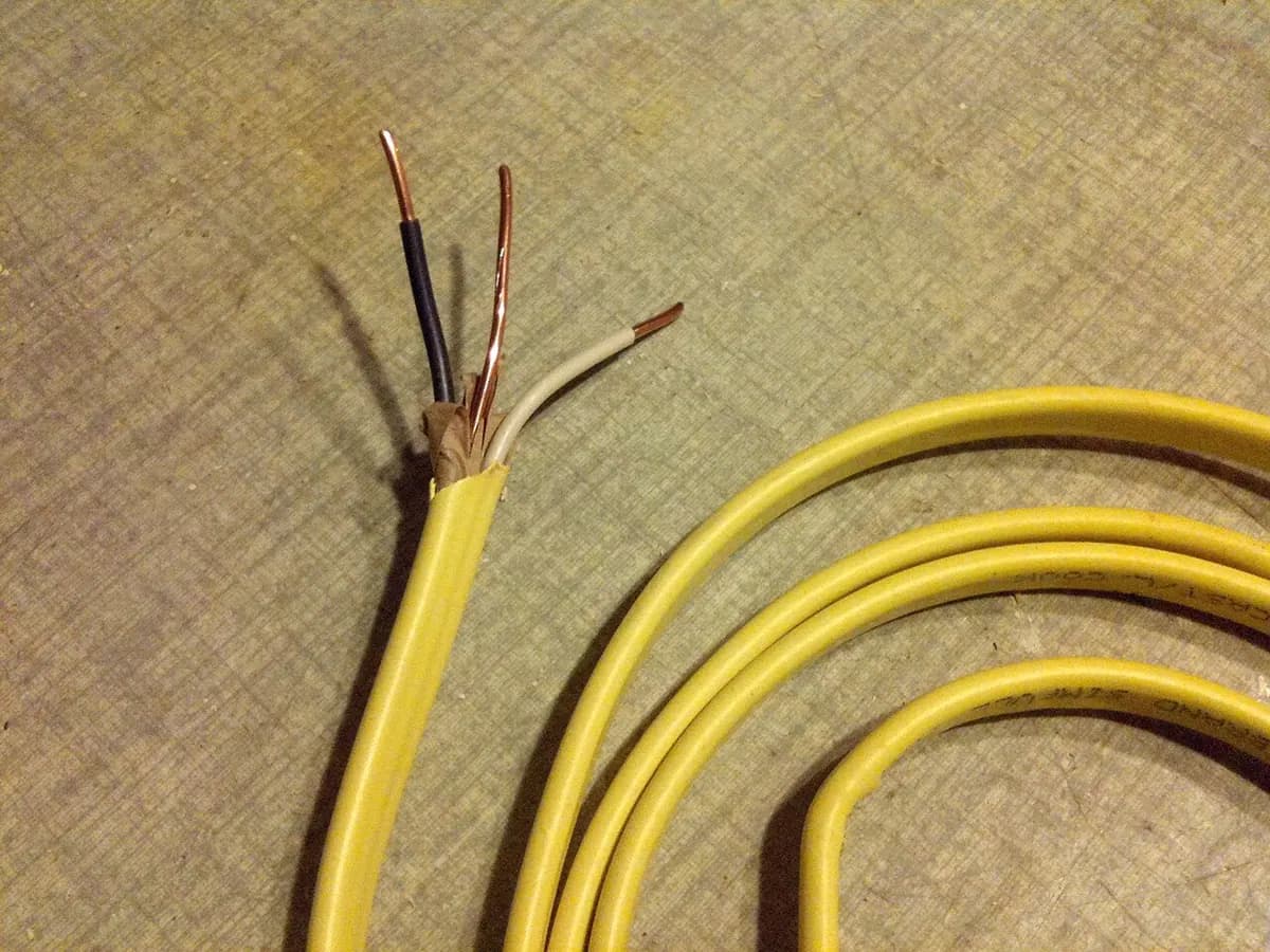 Yellow plastic-jacketed electrical cable with the jacket cut back to show the wires inside.