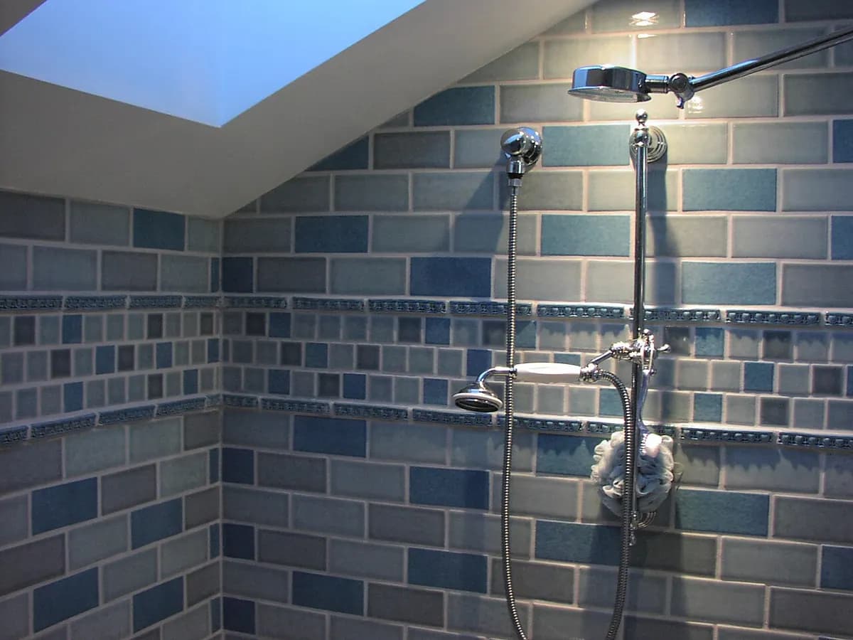 A shower with blue ceramic wall tile and two shower heads on a chrome pipe.