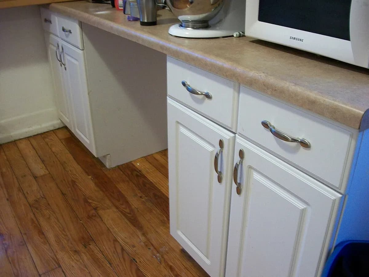 Newly installed white kitchen cabinets with drawers and a countertop, beside a new wood-look floor.