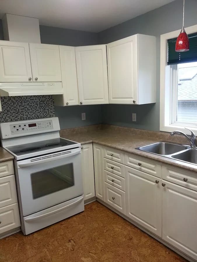 A finished kitchen with white cabinets, a white range, a double sink and a window.