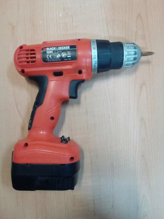 A red and black cordless drill with a battery pack, lying on a light surface.