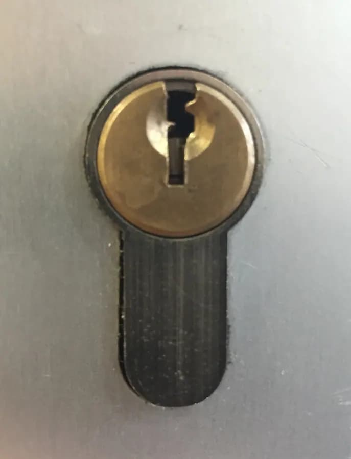 A brass lock cylinder with a keyhole, set into a metal plate.