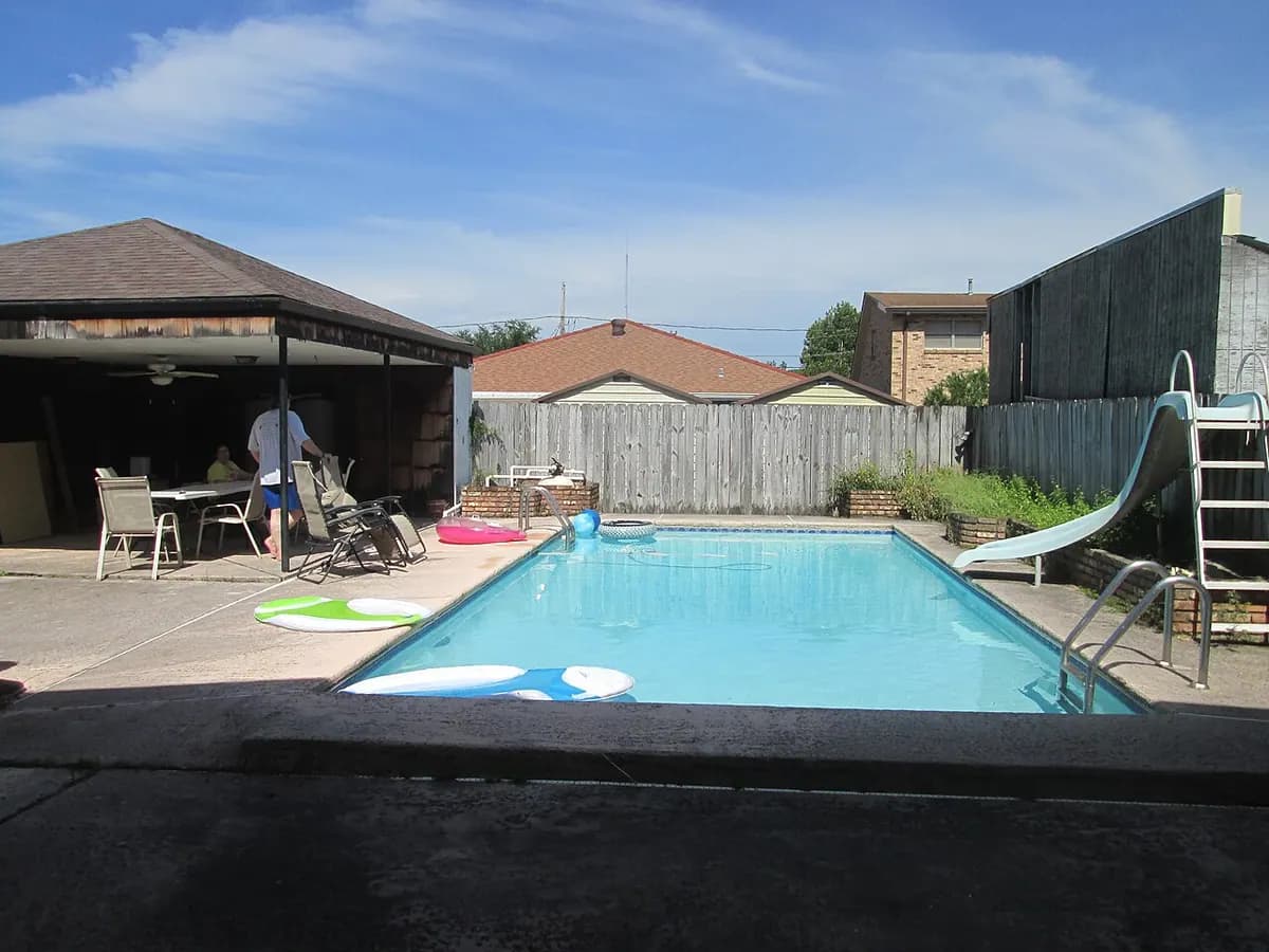 A rectangular backyard pool with a slide, a patio and lounge chairs.