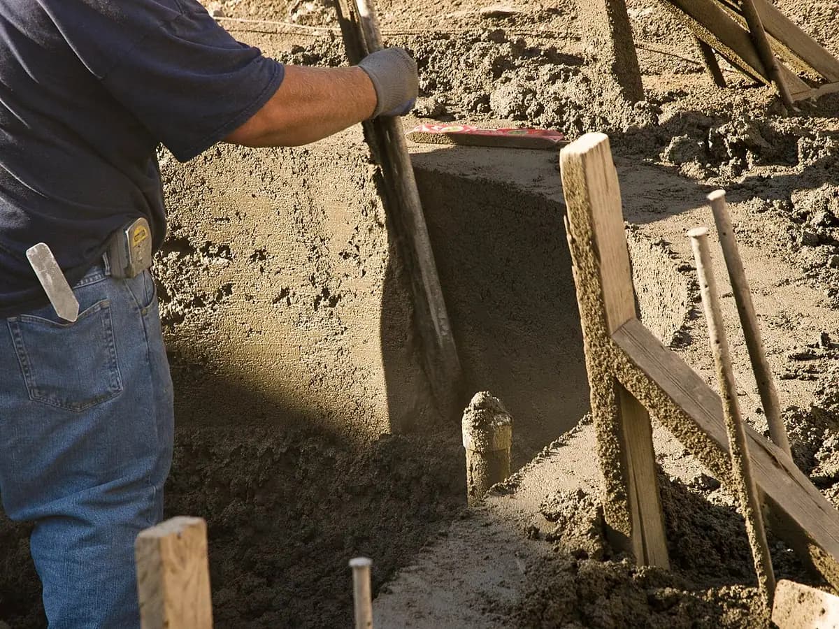 A pool excavation with wooden forms and a worker's arm at the edge of the pit.