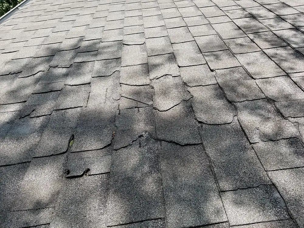 Close-up of weathered asphalt shingles with cracked and lifted tabs.
