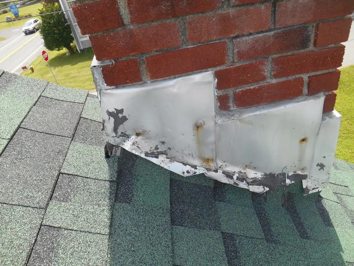 Metal flashing around the base of a brick chimney on a shingled roof, bent and pulling away.