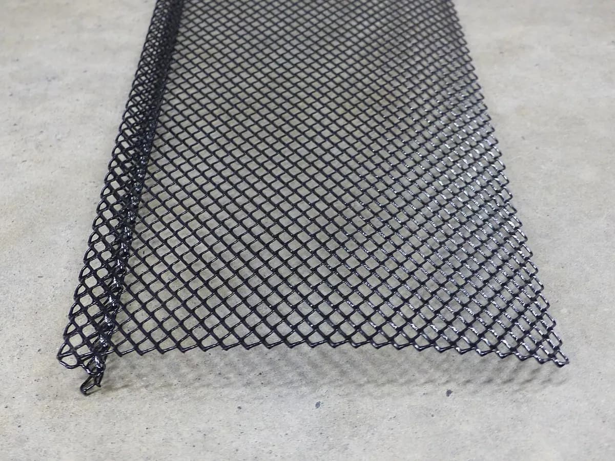 A black mesh gutter guard laid flat on a concrete floor.