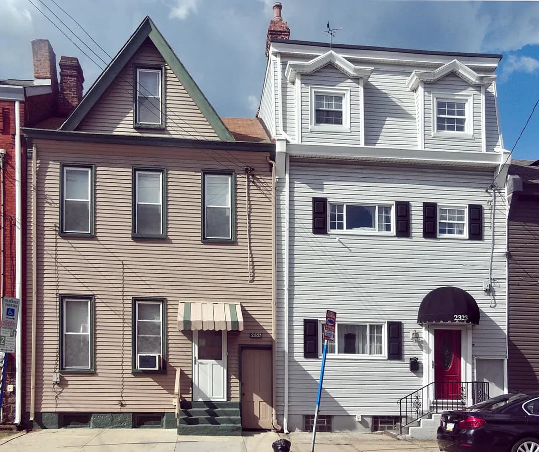 Two row houses covered in vinyl siding, tan on the left and white on the right.