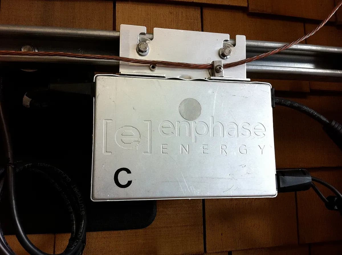 A small gray microinverter box mounted on a rail beneath a solar panel.