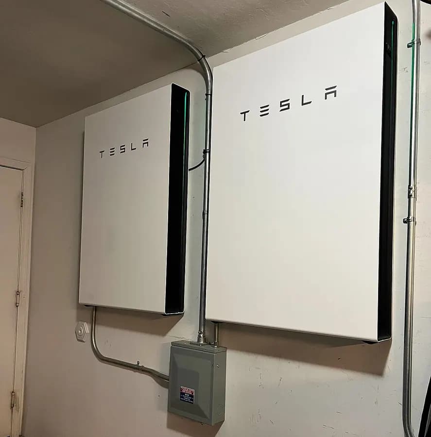 Two white wall-mounted home batteries on the wall of a utility room.