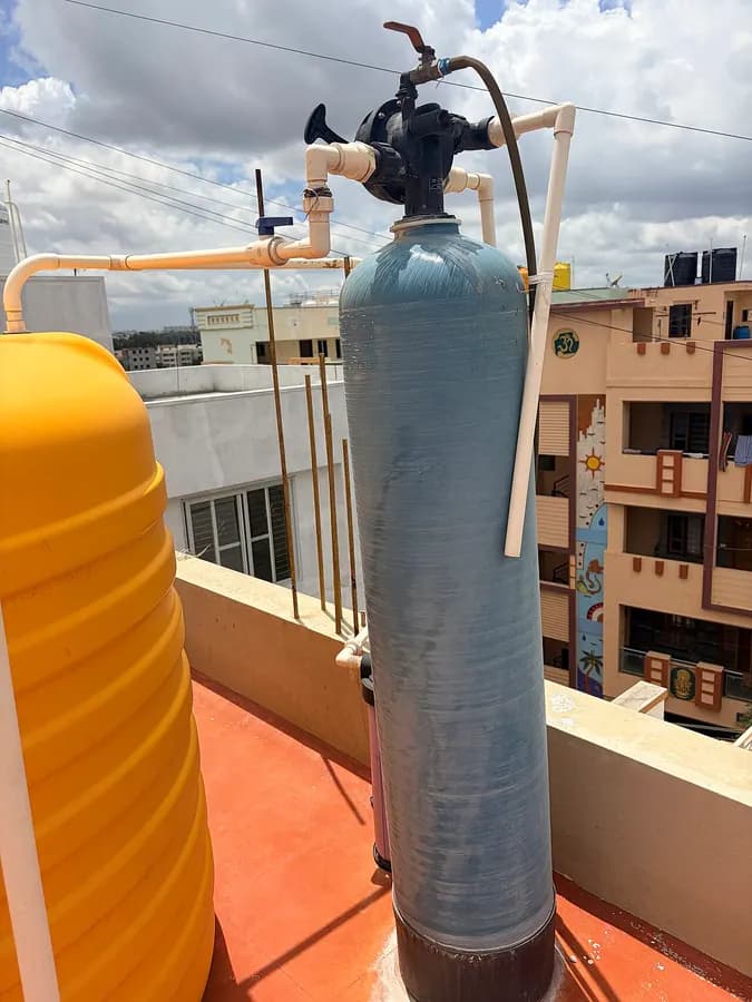 A blue pressure tank with a control valve on top, standing on a rooftop terrace.