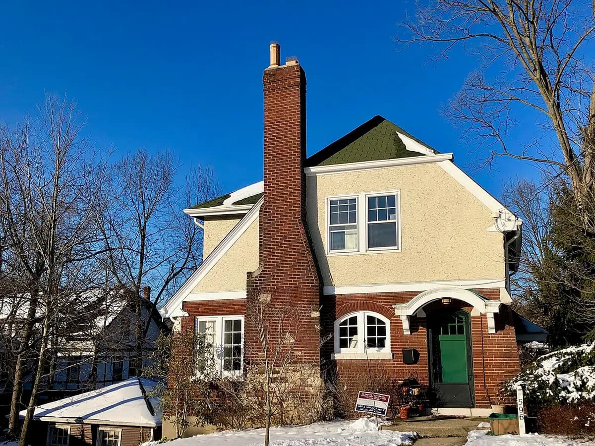 A two-story brick house with a tall brick chimney against a blue sky.