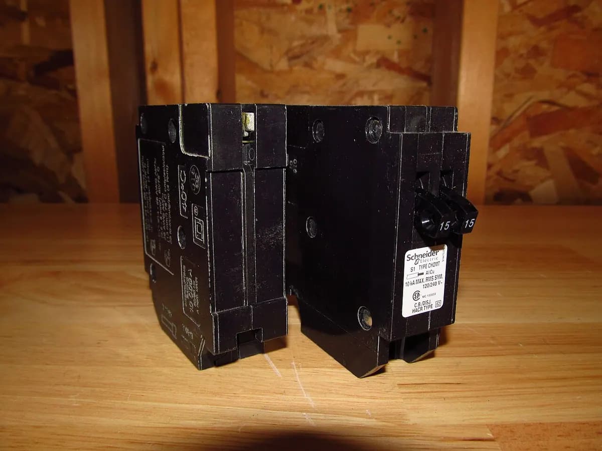 Two black circuit breakers standing side by side on a wooden shelf.