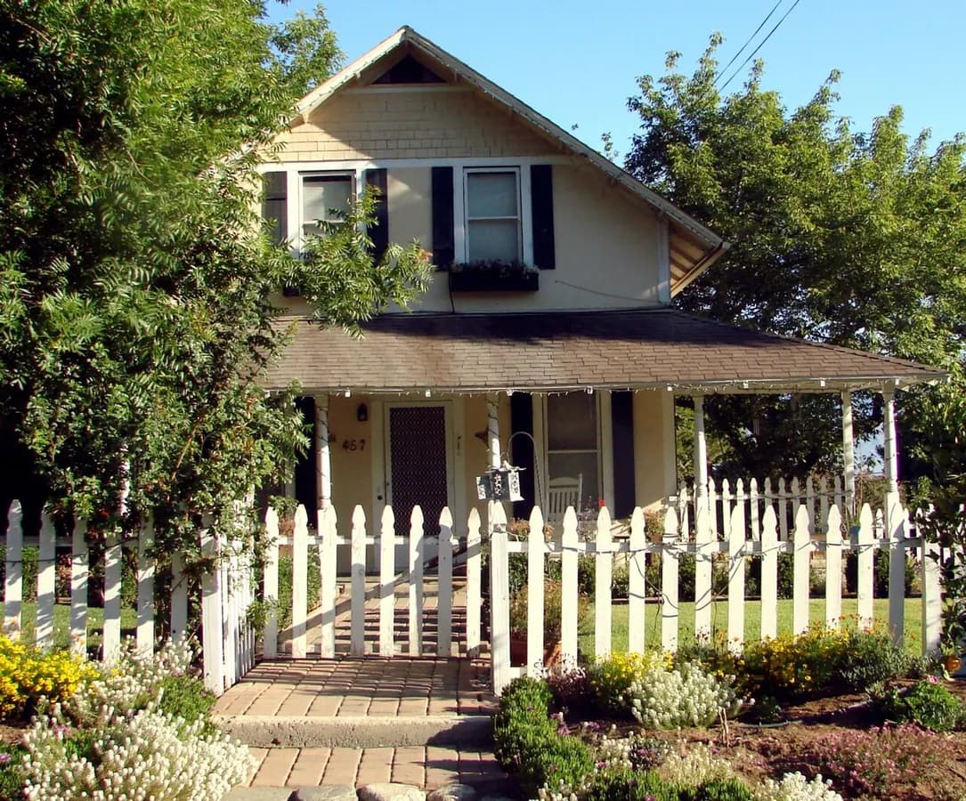 A white wooden picket fence in front of a house with a covered porch.