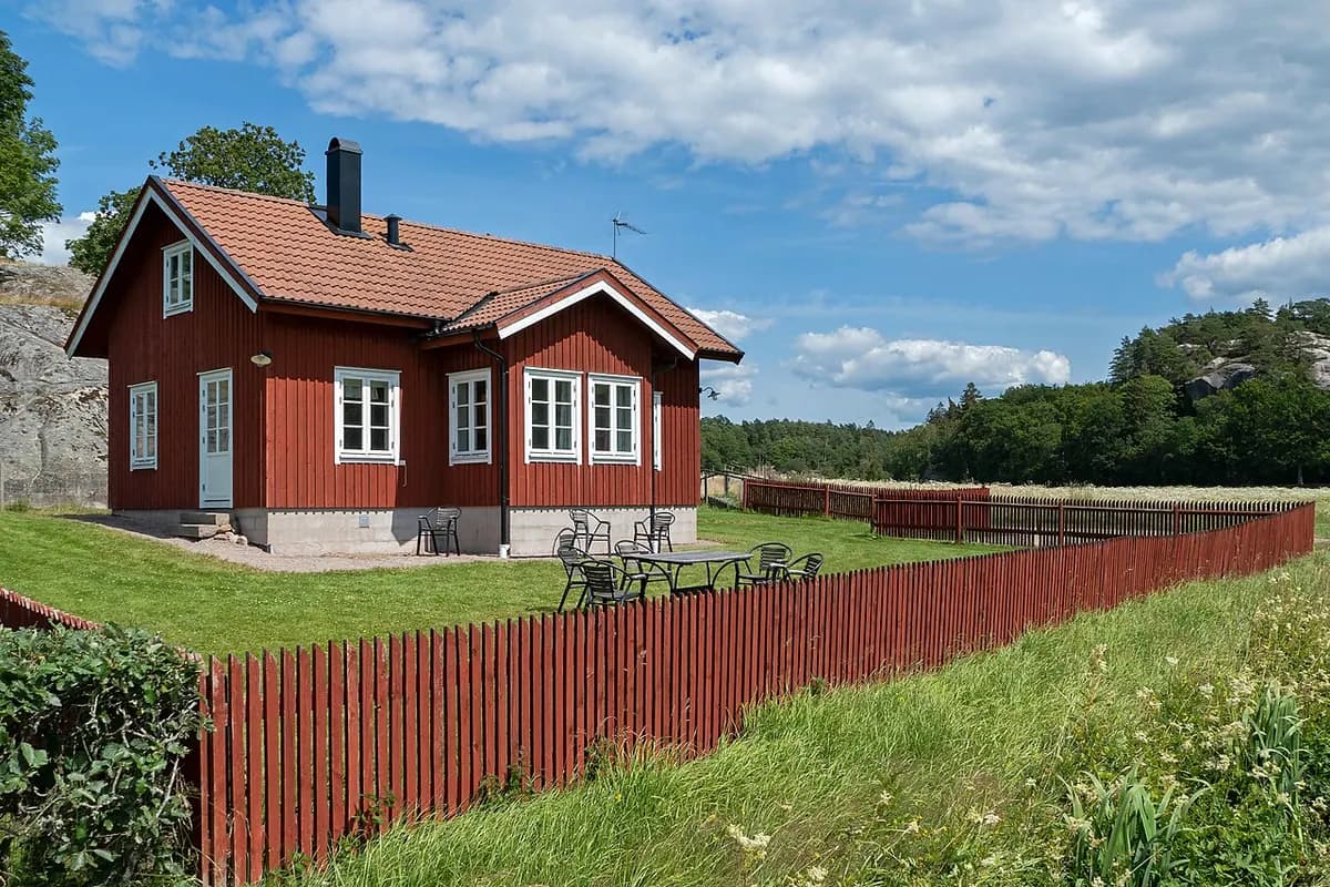 A tall red-painted wooden board fence beside a lawn and a small red house.
