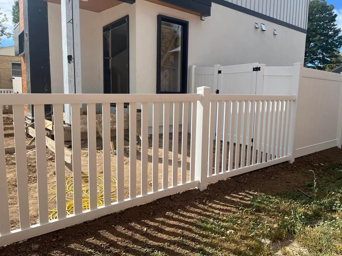 A white vinyl fence with a picket-style rail in front and a solid privacy panel behind it.
