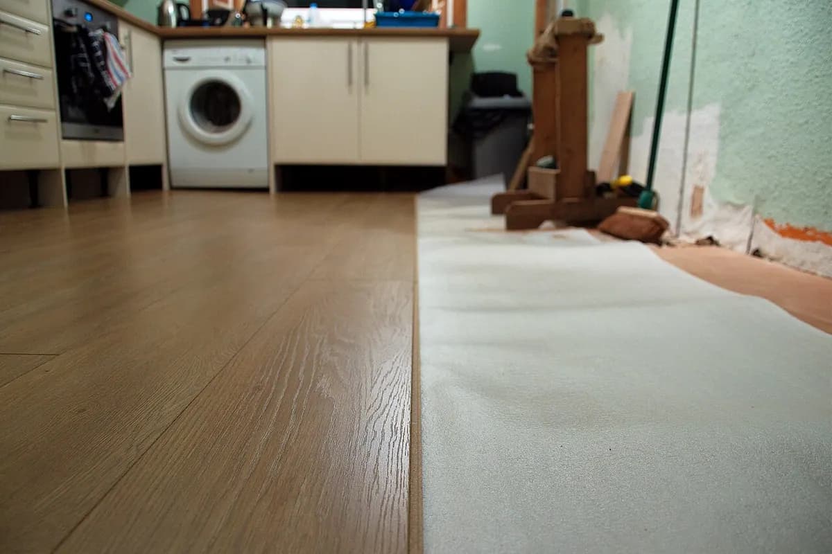 A kitchen floor with new wood-look planks laid over white foam underlayment next to a washing machine.