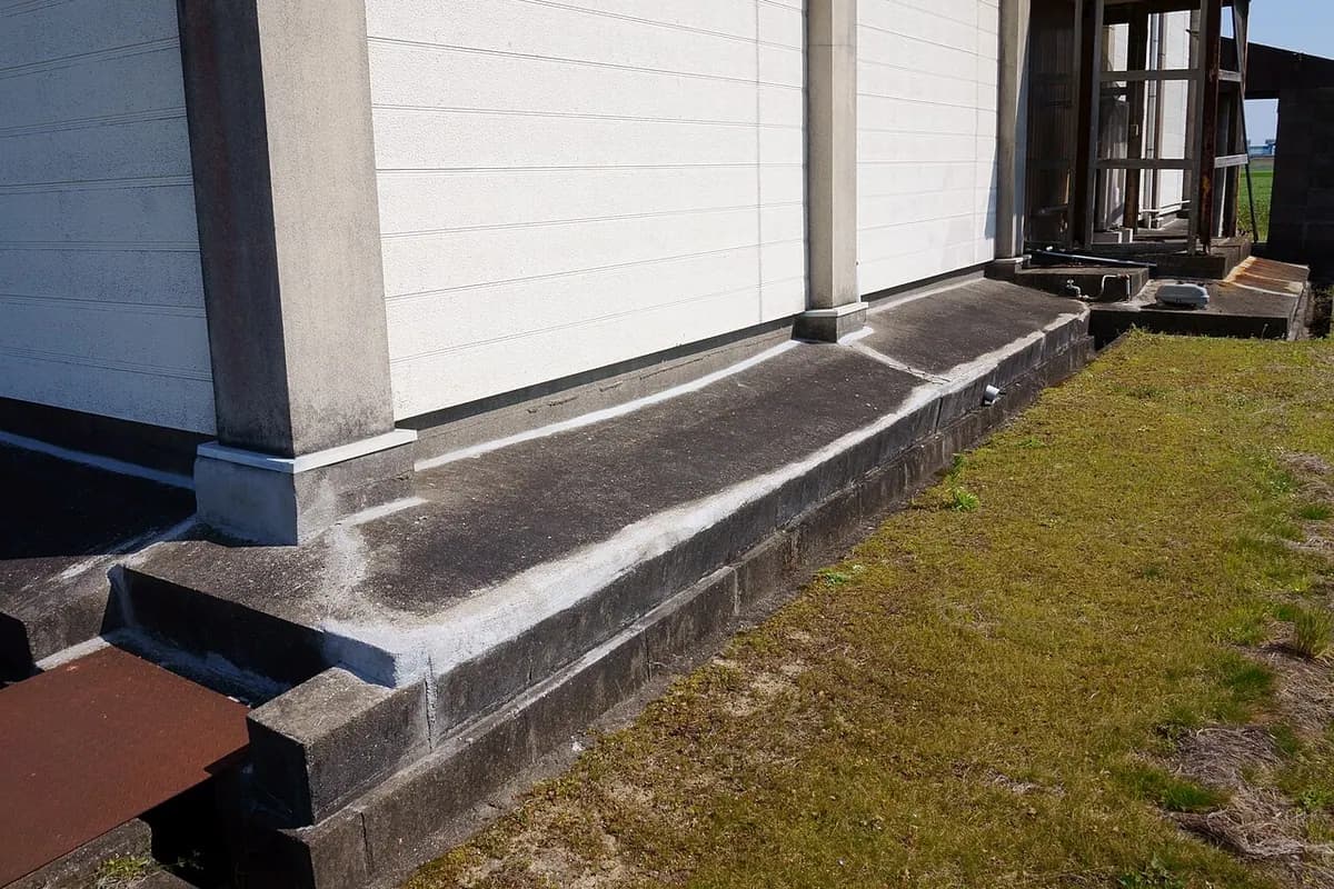 The base of a white building wall with a dark strip of sealant along the concrete foundation edge.