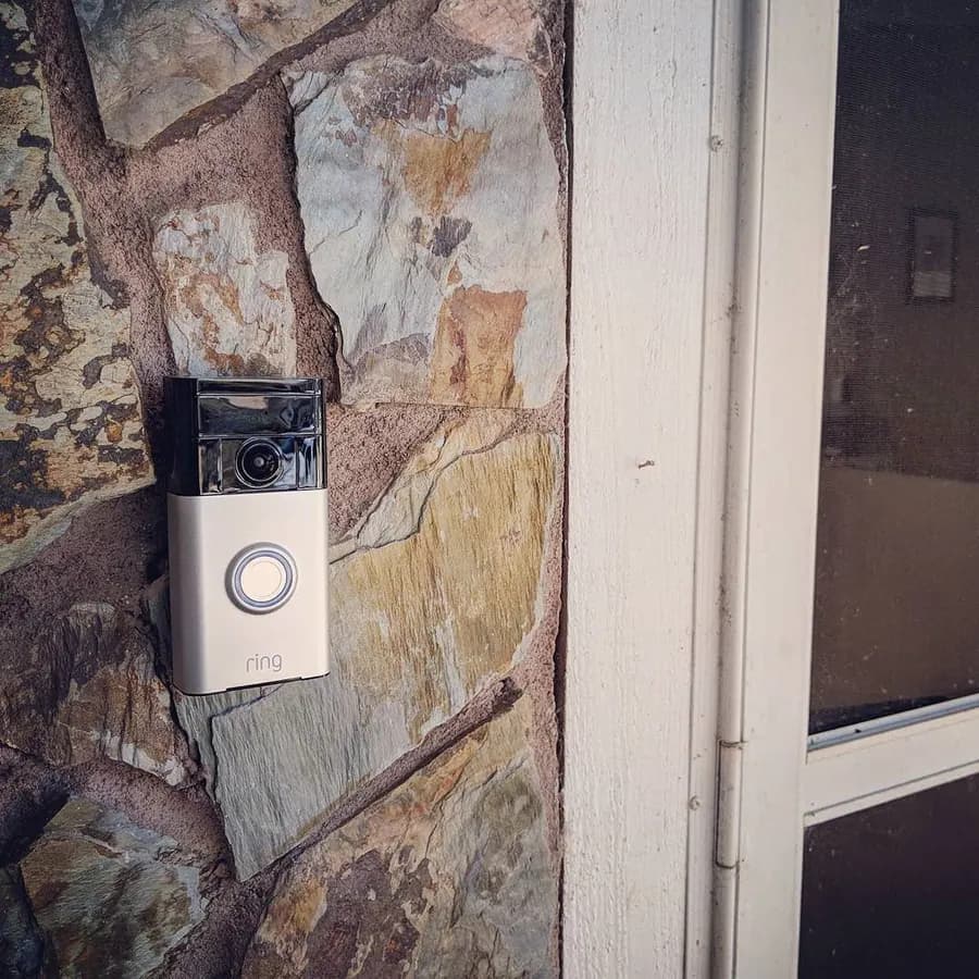 A video doorbell mounted on a stone wall beside a door frame.