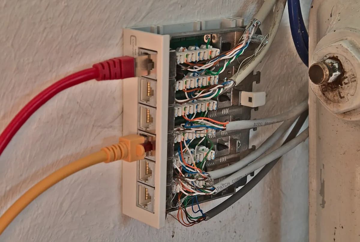 A wall-mounted network patch panel with colored Ethernet cables plugged into six ports.